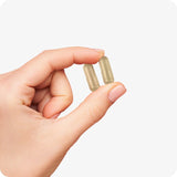 Conceive Plus Ovulation Pack - Fertility + Ovulation Supplements showing a close-up of a hand holding two beige vegan capsules from the Ovulation Support bottle, isolated on a clean white background.