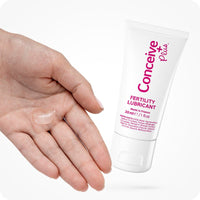 For Conceive Plus Try Me Size Fertility Lubricant Bundle, the image shows a 30ml Conceive Plus lubricant tube positioned beside an open hand with a small amount of gel on its palm, highlighting the texture and application method. The white tube features pink branding and ingredient details, set against a clean white background.